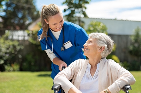 A nurse pushing an elderly woman in a wheel chair.