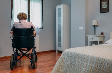An elderly person in a wheel chair looking out of a window.